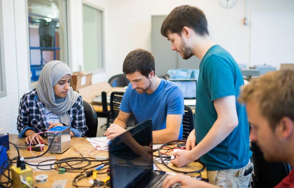 Students working together on a hands-on computing project in a lab setting, with a caption describing Grand Valley State University's School of Computing offering knowledge and real-world experience to undergraduates in a tech-driven world, fostering inno